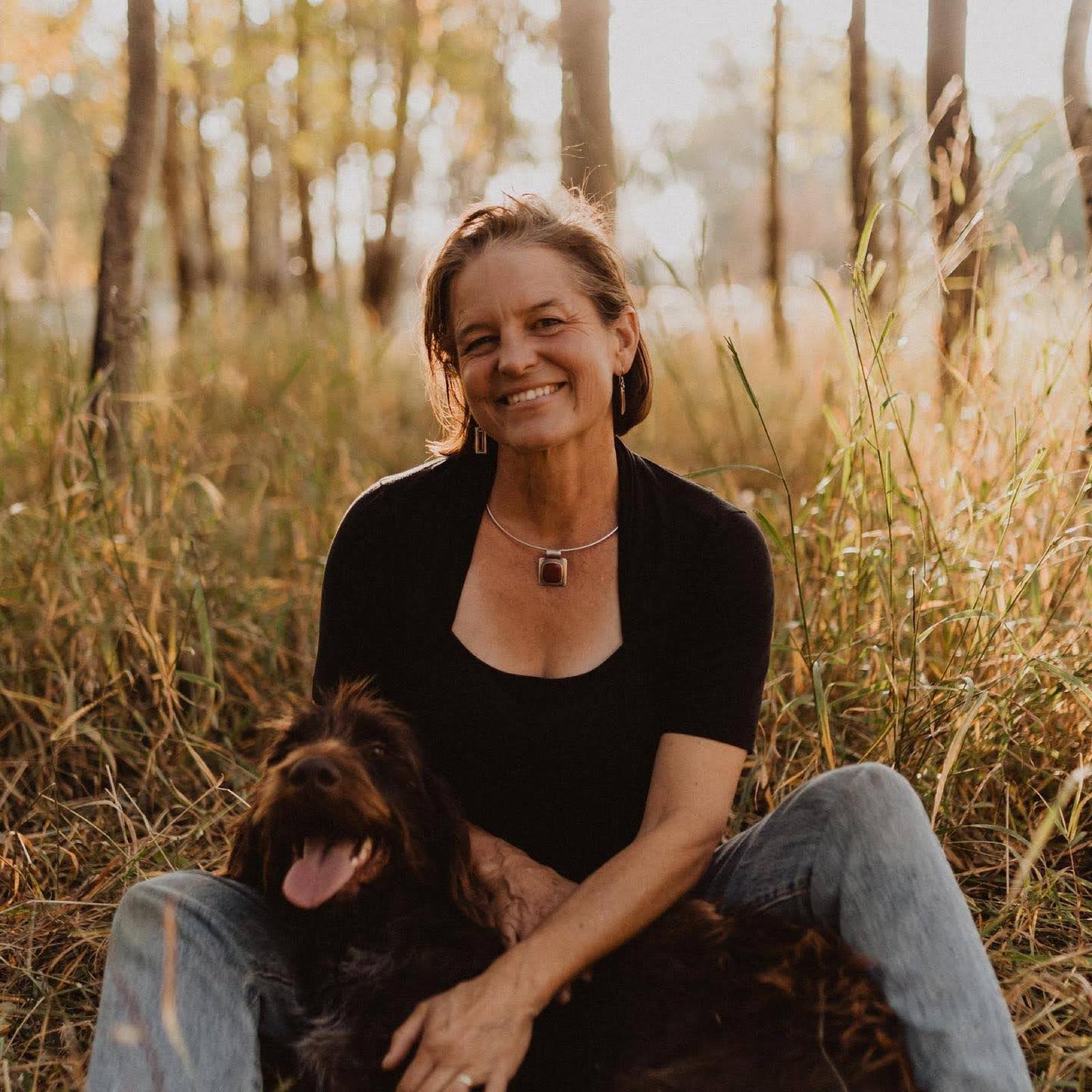 Lorca sitting in tall autumn grass among aspens, her dog leaning into her lap