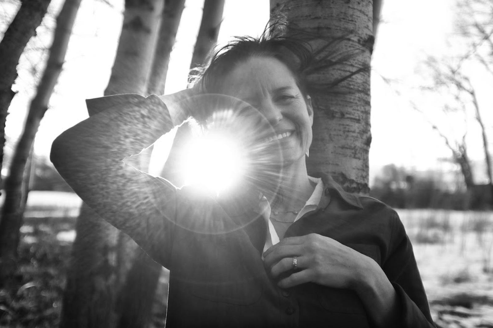 Lorca among aspen trunks, sunlight flaring through her raised arm