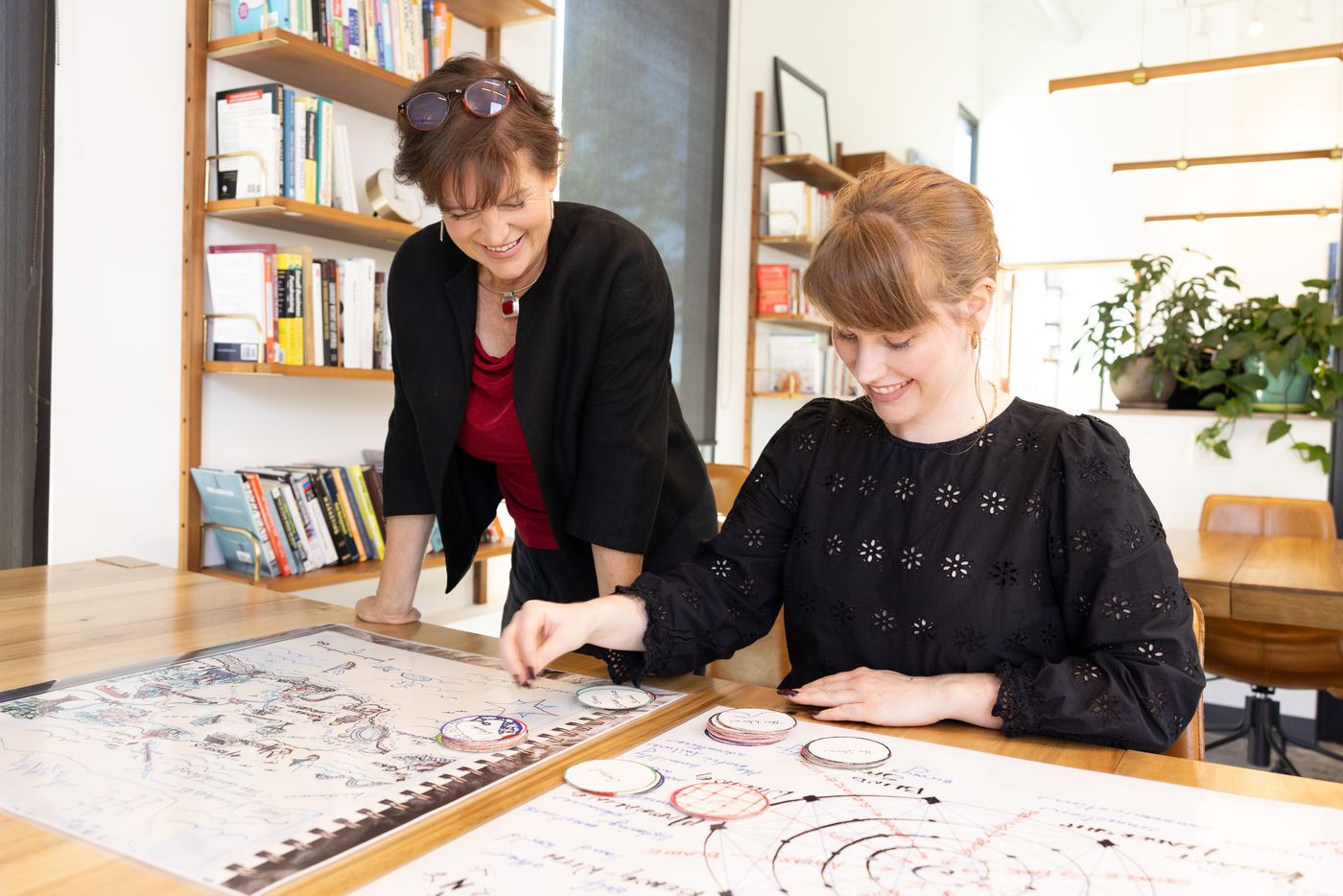 Lorca leaning over a large hand-drawn tarn map spread across a table, working through it with a client