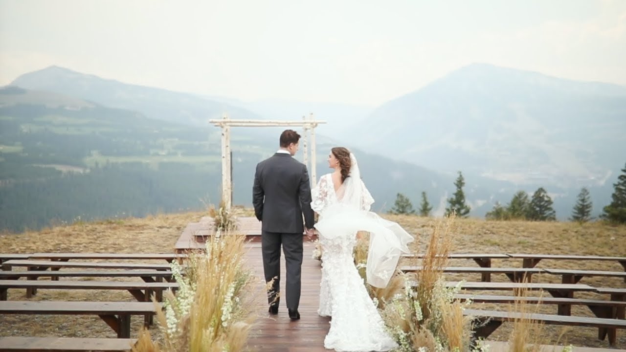 A bride and groom walking back down a wooden aisle after their ceremony, an arch of birch behind them and the Montana range beyond